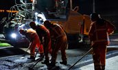 Mannen in oranje pakken asfalteren 's nachts de weg.